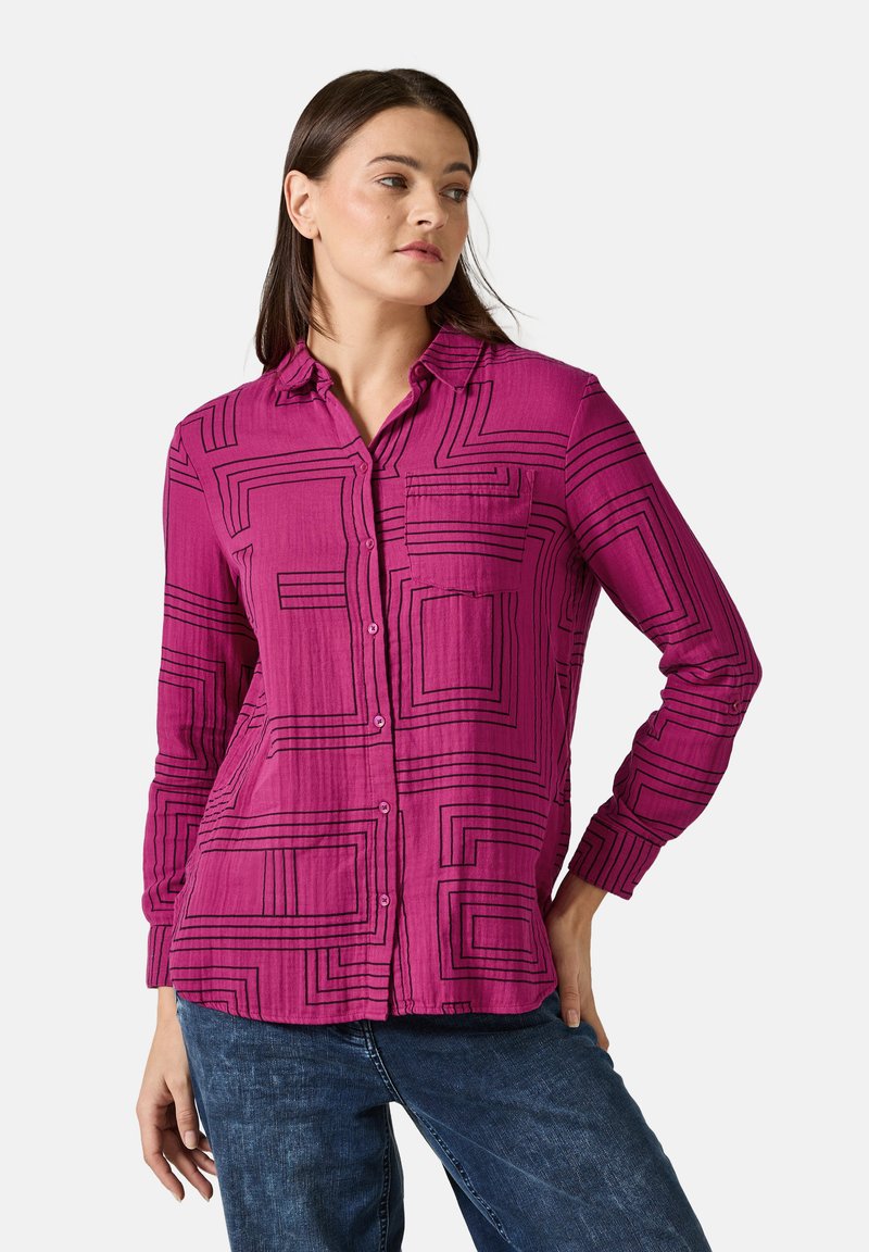 Camicia fucsia a maniche lunghe con bottoni, decorata da un motivo geometrico nero, con colletto e taschino sul petto; il tessuto sembra leggero e testurizzato.