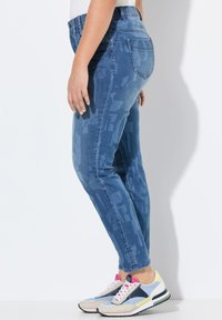 Džínové kalhoty s přiléhavým střihem, v modrém odstínu a s jemným abstraktním vzorem. Doplněné o vícebarevné sportovní tenisky.