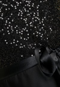 Tissu noir orné de sequins brillants, avec un ruban satiné lisse noué à la taille, offrant une surface texturée et réfléchissante.