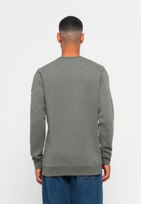 Grå crewneck genser laget av mykt stoff med lange ermer, ribbede mansjetter og rett hem. Ingen synlige logoer eller mønstre.