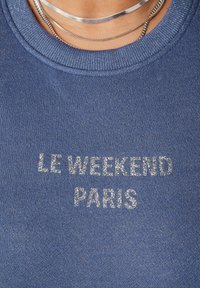 Blauwe sweatshirt met een textuurafwerking. Voorzien van de zilveren tekst "LE WEEKEND PARIS" prominent op de voorkant. Geribbelde ronde halslijn.