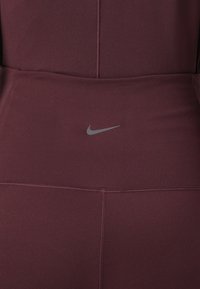 Burgundske atletske tajice s visokim pojasom, siva Nike oznaka i ravni šavovi za glatku završnicu. Elastični, lagani materijal.