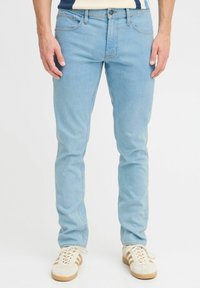 Jeans in denim blu chiaro con una vestibilità slim, caratterizzati da cuciture a contrasto, tasche frontali e chiusura con bottone. Abbinati a sneakers bianche.