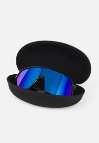 Gafas de sol con una gran lente espejo azul en un estuche rígido negro y texturizado. La montura es elegante, con elementos de diseño angulares y deportivos.