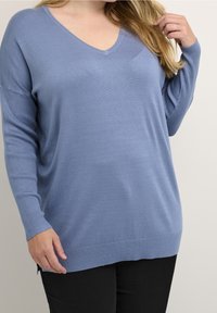 Niebieski sweter w serek wykonany z miękkiego materiału dzianinowego, z ribbowanymi rękawami i ribbowanym dołem, w luźnym kroju oraz z bocznymi rozcięciami na dole.