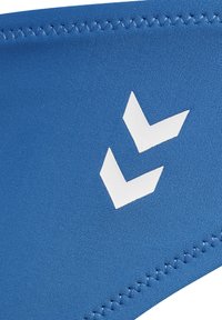 Niebieska elastyczna opaska na głowę z białym logo w wzór chevron. Materiał ma gładką strukturę, a brzegi są starannie wykończone.