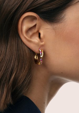 Pendientes de aro de oro con piedras preciosas de colores en un arreglo floral, mostrando un acabado pulido y detalles intrincados sobre la piel.