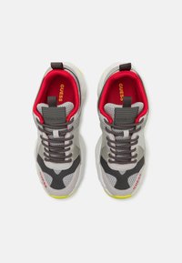 Las zapatillas cuentan con una parte superior de malla gris con acentos negros, forro rojo y una etiqueta de marca texturizada en gris. Detalle amarillo en la suela. Diseño con cordones.