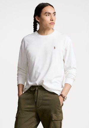 Witte blouse met lange mouwen, een ronde halslijn en een klein geborduurd logo. Gecombineerd met olijfgroene cargobroek. Soepele stoftextuur.
