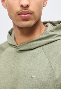 Gros plan d'une personne portant un sweat à capuche Nike vert clair, montrant le bas du visage, le cou et le haut de la poitrine avec un petit logo Nike swoosh.