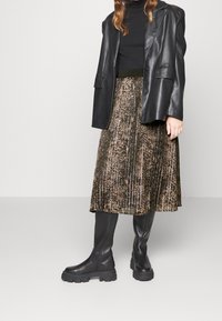 Svart läderöversize blazer över en figurnära svart topp, i kombination med en plisserad knälång kjol med brun och svart mönster, samt knähöga svarta stövlar.