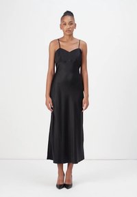 Black satin slip dress with thin straps, a slight v-neck, and a smooth texture, falling to mid-calf. Worn with black high heels.