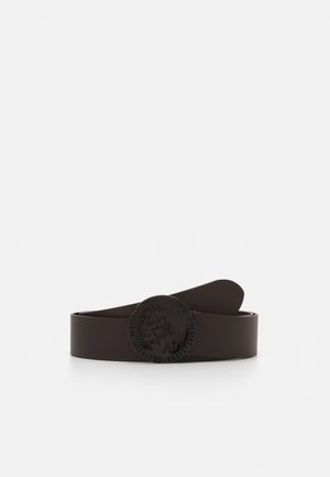 Ceinture en cuir brun foncé enroulée avec boucle ronde noire présentant un profil en relief du visage d'un homme et un texte de marque.