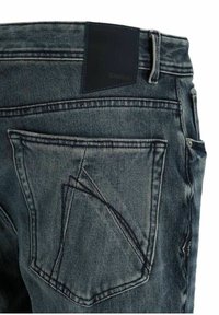 Bolsillo trasero y cinturilla de unos vaqueros de mezclilla azul oscuro con parche de marca de cuero negro y detalle de costura en el bolsillo en ángulo.