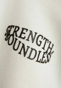 Tela blanca con bordado texturizado en negro, que muestra las palabras " FUERZA SIN LÍMITES" en un diseño curvado.
