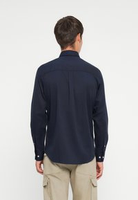 Tumši zila krekls ar garām piedurknēm un apkakles izgriezumu, ar taisnu apakšmalu un pogājamiem aprocēm, izgatavots no mīksta auduma komfortam.