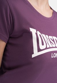 Purple cotton T-shirt with short sleeves featuring a large white "LONSDALE" logo across the chest and a smooth, soft texture.