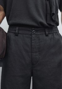 Pantaloni in lino neri, leggeri, con una vestibilità rilassata, vita elasticizzata e chiusura con un singolo bottone. Tessuto testurizzato con una leggera lucentezza.