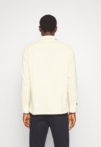 Kremowa koszula z długim rękawem, kołnierzykiem zapinanym na guziki i mankietami zapiętymi na guziki. Gładka faktura, prosty krój, bez widocznych wzorów czy akcentów.