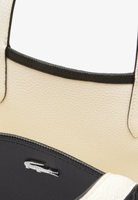 Sac fourre-tout en cuir crème texturé avec des finitions noires, muni d'une doublure intérieure lisse et d'un subtil détail de logo. Design élégant et fonctionnel.