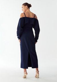 Námořnické modré šaty s odhalenými rameny, přiléhavým tělem a dlouhou sukní s rozparkem na zadní straně. Hladká látka a minimalistické designové detaily.