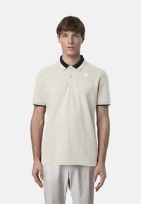 Polo shirt beige chiaro con colletto navy, maniche corte e una texture sottile. Presenta un piccolo logo sul petto e bottoni sul collo.