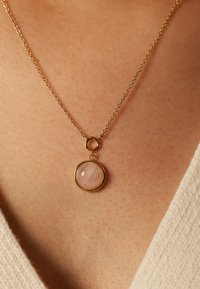 Collier en chaîne dorée avec un pendentif en quartz rose circulaire à surface lisse, suspendu à un petit maillon circulaire.
