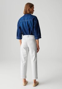 Chemise en denim bleu foncé à manches boutonnées, assortie à un pantalon blanc à revers et des chaussures slip-on beiges. Look simple et décontracté.