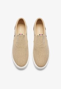 Beige instappers van textiel met een witte rubberen zool. Versierd met een klein gestreept label op de wreef en een bruine hielafwerking.