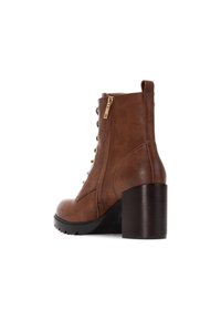 Botín de cuero marrón hasta el tobillo con un acabado suave, cremallera lateral, tacón elevado y cordones en la parte delantera. Suela texturizada para tracción y estabilidad.