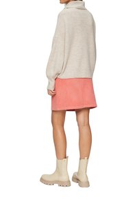 Beige rib gebreide trui met een hoge hals, gecombineerd met een roze corduroy minirok en crèmekleurige enkellaarsjes met dikke zolen.