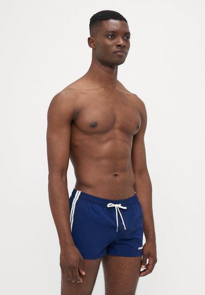 Shorts de bain navy avec des rayures blanches sur les côtés et une ceinture à cordon, fabriqués dans un tissu léger et lisse, avec une coupe courte.