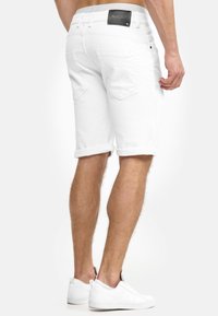 Witte denimshorts met opgerolde pijpen, twee achterzakken en een leren patch op de tailleband. De stof heeft een gladde, gestructureerde uitstraling.