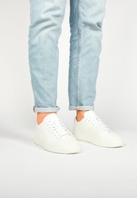 Baskets blanches en cuir au design bas, avec des lacets plats et des semelles en caoutchouc texturé. Portées avec un jean en denim bleu clair retroussé.