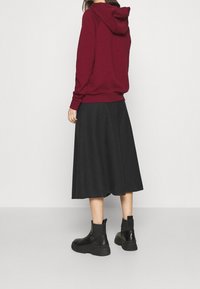 Burgundy hoodie med huva, i kombination med en svart kjol som går till knäna och svarta ankelstövlar. Slät tyg och figurnära siluett.