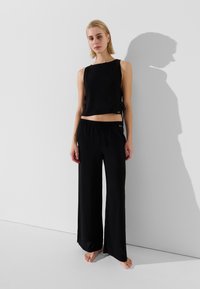 Fekete, ujjatlan, cropped top, oldalsó megkötőkkel, párosítva laza fekete, bő szárú nadrággal. Puha textúra, minimális márkázás látható a ruhákon.