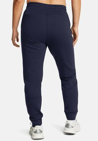 Marineblaue Sweatpants mit elastischem Bund, schmal zulaufenden Beinen und seitlichen Einsätzen. Kombiniert mit weißen und silbernen Laufschuhen.