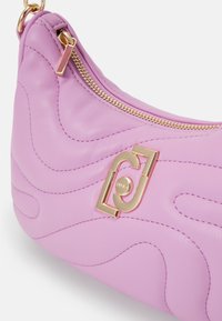 Sac à main en cuir rose avec une texture en vagues, une fermeture éclair dorée et un accent logo géométrique proéminent à l'avant.