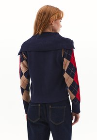 Maglione a maglia blu navy con maniche a forma di diamante in contrasto nei colori rosso, beige e blu navy. Collo e orlo a costine, silhouette aderente.