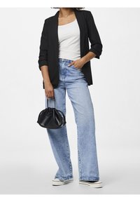 Černý blazer přes bílý top bez rukávů, doplněný světlomodrými širokými džínami a malou černou kabelkou. Hladké materiály, ležérní design.