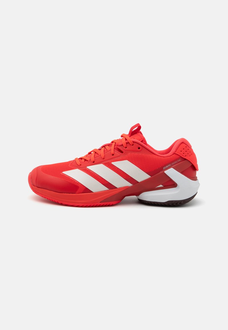 Red athletic shoe with white three-stripe design, mesh upper, rubber sole, and padded collar. Includes a sturdy heel and textured surface.