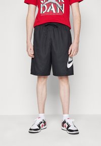 Black athletic shorts with an elastic waistband and side logo. Paired with a red graphic t-shirt and black and white sneakers.