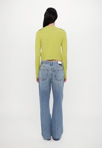 Lime green cropped sweater with long sleeves and shoulder details paired with light blue wide-leg jeans featuring two back pockets.
