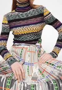 Col roulé en tricot rayé dans diverses couleurs associé à une jupe plissée à motifs présentant des designs linéaires et de grille dans des couleurs vives.