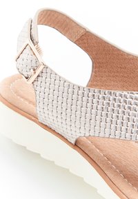 Sandal in tessuto grigio chiaro con tomaia testurizzata, fibbia regolabile e soletta ammortizzata su una suola bianca stratificata.