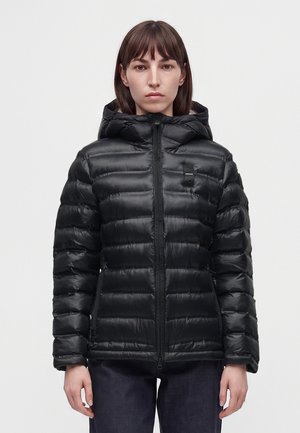 Woman facing forward wearing a black hooded puffer jacket with horizontal quilting and zipped front against a plain background.
