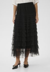 Black tiered tulle skirt with ruffled layers, a fitted waistband, and a sheer, flowy texture. Paired with patent leather slingback heels.