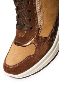 Braune Wildleder-Sneaker mit einer sandfarbenen Zehenkappe, metallisch bronzefarbenen Akzenten, kontrastierenden Nähten und einem seitlichen Reißverschluss. Runde Schnürsenkel in Dunkelbraun.
