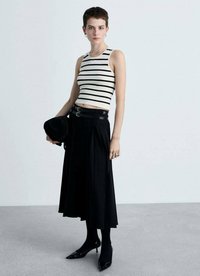 Prúhované crop top v krémovej a čiernej farbe, spárované s čiernou plisovanou sukňou. Modelka má na sebe čierne vysoké podpätky a drží čierny klobúk. Predvedené strieborné doplnky.