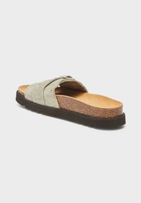 Green suede slide sandal with cross straps, textured footbed, cork midsole, and rubber outsole; features gold studs on the straps.